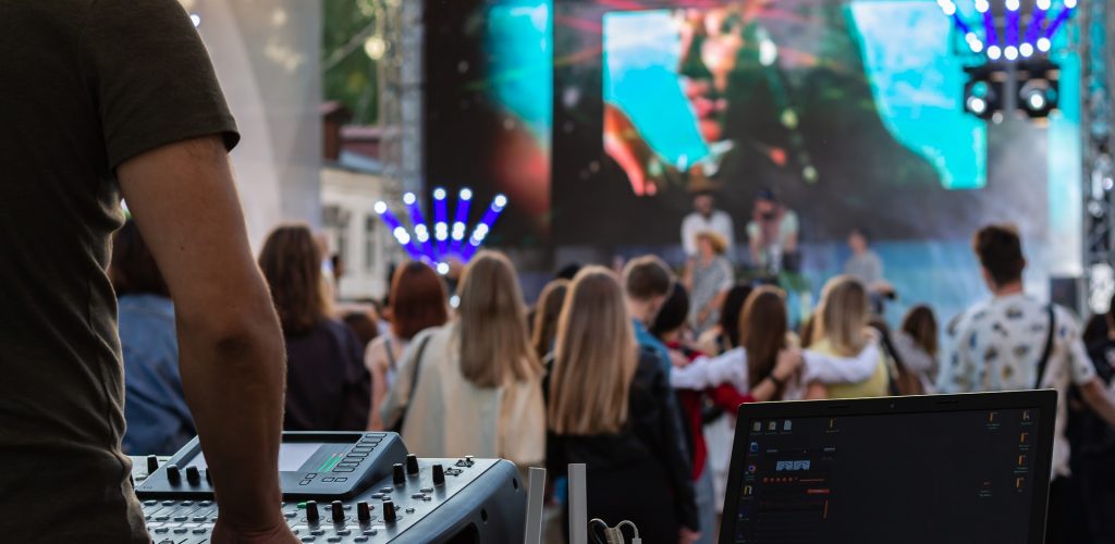 Dj mixing, laptop outdoors at party festival with crowd of people in background. Fun, summer, youth, nightlife, music and entertainment concept. low light. selective focus. professional DJ music mixer